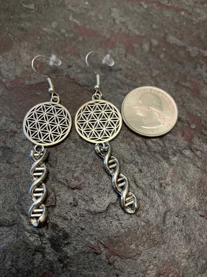 May include: Silver earrings featuring a flower of life design and a DNA helix drop. The earrings are approximately the size of a 25 pence coin.