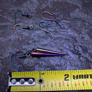 May include: A pair of rainbow iridescent earrings with a pointed design. The earrings are approximately 1 3/8 inches long. The earrings are shown next to a measuring tape.