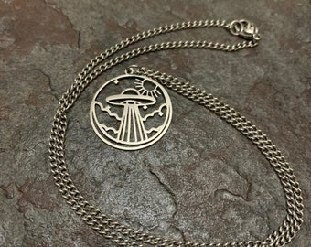 May include: A silver chain necklace with a circular pendant featuring a UFO, stars, and a sun. The pendant is cut out, creating a silhouette effect.