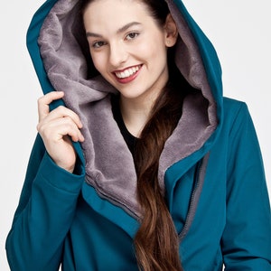May include: A teal hooded coat featuring a soft, grey fleece lining inside the hood. The coat includes a matching teal fabric belt tied at the waist and a full-length front zipper closure, providing a structured look with long sleeves.