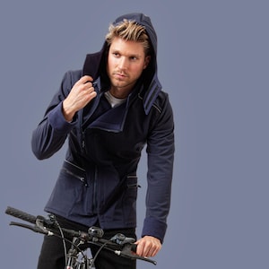 Pode incluir: Casaco azul marinho com capuz com gola e punhos em azul escuro contrastantes. O casaco apresenta fecho de correr, vários bolsos e um design elegante e moderno. A pessoa está segurando um guidão de bicicleta.