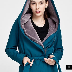 May include: A teal hooded coat featuring a soft, greyish-purple faux fur lining, a wrap-style front with a matching tie belt, and a zipper closure. The garment is shown with a color palette swatch on the left and the brand name ILLEOLLA in the corner.
