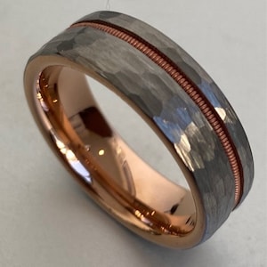 Op de afbeelding: Een zilveren ring van wolfraam met een gehammerde afwerking en een dunne roosgoud band rond het midden.