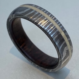 May include: A silver and white patterned ring with a dark wood inlay. The ring has a thin white stripe running around the centre.