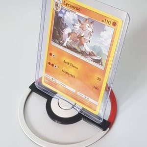 Op de afbeelding: Een Pokémon-verzamelkaart met Lycanroc, weergegeven in een doorzichtige beschermhoes. De kaart staat op een witte, zwarte en rode cirkelvormige standaard, die lijkt op een Poké Ball. De kaart heeft een oranje achtergrond met een wolfachtig wezen.