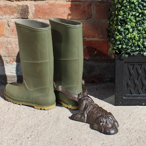 May include: Olive green rubber boots with a brown frog boot scraper. The boots are tall and have a simple design. The frog boot scraper is detailed and adds a decorative touch to the outdoor setting.