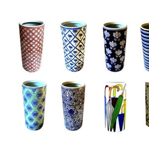 May include: Eight decorative ceramic umbrella stands with various patterns. Designs include red plaid, blue palm trees, white flowers on navy, blue and white stripes, green and blue geometric shapes, blue floral, umbrellas, and red roses.