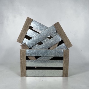 Könnte beinhalten: Eine rechteckige Aufbewahrungskiste aus horizontalen, verzinkten Metalllatten und braunen Holzeckpfosten. Die Kiste verfügt über ein offenes Lamellendesign mit sichtbaren Lücken zwischen den Metallpaneelen, das eine Kombination aus industriellen Metall- und natürlichen Holztexturen aufweist.
