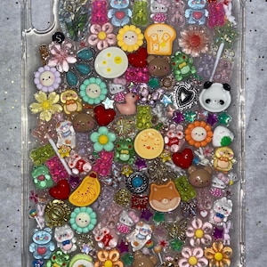 Puede incluir: Funda transparente para tableta decorada con una variedad de dijes coloridos en miniatura. Los dijes incluyen flores, osos, corazones y otros diseños lindos. La funda está llena de una variedad de colores y texturas, creando una estética lúdica y caprichosa.
