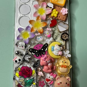 May include: Clear phone case decorated with various charms, including flowers, a teddy bear, a slice of toast, a butterfly, and hearts. Other charms include a stained glass rose, a moon with a bear, and several cartoon characters.