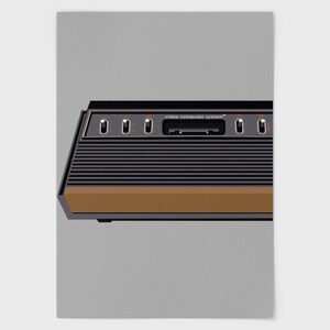 Può includere: Illustrazione di una console per videogiochi retrò. La console è nera con un accento marrone e linee orizzontali. Il testo "video computer system" è stampato in alto. Presenta pulsanti e uno slot per cartucce.