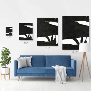 May include: Four black and white abstract art prints in different sizes, displayed on a white wall above a blue sofa. The prints feature bold, gestural strokes and a minimalist aesthetic.