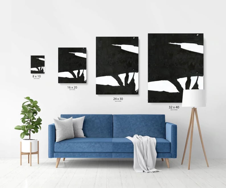 May include: Four black and white abstract art prints in different sizes, displayed on a white wall above a blue sofa. The prints feature bold, gestural strokes and a minimalist aesthetic.