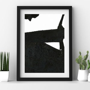 May include: Black and white abstract art print in a black frame. The artwork features bold, textured black shapes against a white background. The framed art is displayed on a white shelf with potted plants.