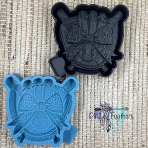 May include: Two baseball-themed cookie cutters. One is black, the other is blue. Each cutter features a baseball, a bow, and baseball bats. The cutters are designed to create baseball-themed cookies or treats.