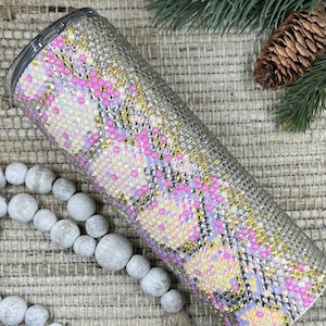 May include: A stainless steel tumbler with a pink, white, and gold glitter design. The tumbler is covered in rhinestones.