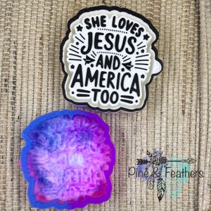 May include: Two decorative items. One is a layered sticker with the text "SHE LOVES JESUS AND AMERICA TOO" in black and white. The other is a blue, purple, and pink resin mold with the same text. The background is a woven texture.