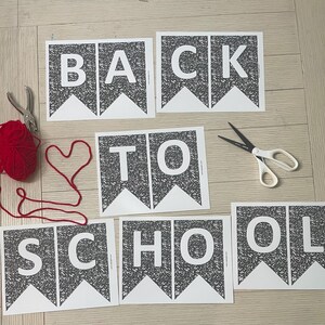 Può includere: Un set di banner stampati con la scritta "BACK TO SCHOOL" in lettere maiuscole bianche su sfondo nero strutturato. Sono presenti anche un gomitolo di lana rosso, delle forbici e un disegno a forma di cuore con il filo.