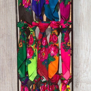 May include: A display of colorful floral scarves. The scarves are arranged on a wooden rack, each showcasing a vibrant design of pink, red, and yellow flowers with green leaves. The background is a light wood-grain texture.