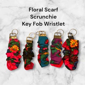 May include: Five colorful floral fabric key fobs with gold key rings. The key fobs are made from a stretchy fabric with a floral pattern and are designed to be used as a wristlet, scrunchie, or key fob.