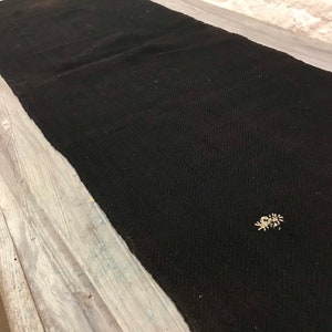 Peut inclure: Un chemin de table noir tissé avec un motif subtil. Le chemin de table est posé sur une surface en bois clair.