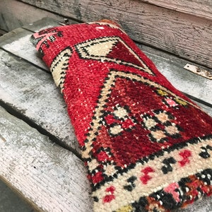 Könnte beinhalten: Ein rotes, weißes und schwarzes Kissen mit traditionellem Muster. Das Kissen ist aus gewebtem Stoff und hat eine rechteckige Form.