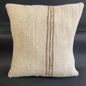 May include: Square beige pillow with three vertical brown stripes. The pillow has a textured, woven appearance. The neutral color palette and simple design make it suitable for various home decor styles.