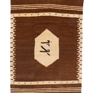 May include: A rectangular brown rug with a central beige geometric shape containing black text. The rug has a border of beige and brown stripes and a zig-zag pattern along the edges. This rug is suitable for home decor.