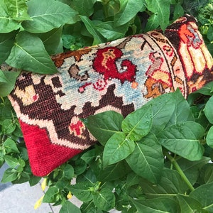 Könnte beinhalten: Ein rotes, braunes und blaues Kissen mit einem Muster und einem Fransenrand. Das Kissen ist aus gewebtem Stoff und hat ein traditionelles Design.