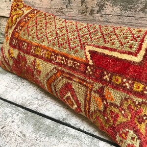 Könnte beinhalten: Ein rechteckiges Kissen aus gewebtem Stoff mit einem traditionellen Muster in Rot, Orange und Beige.