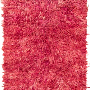 Peut inclure: Un tapis rectangulaire et touffu, dans des tons de rouge et de rose. Le tapis présente un épais velours texturé, avec de longues fibres douces créant un aspect moelleux. La couleur est uniforme, avec des variations de tons.