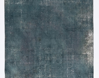 Puede incluir: Una alfombra rectangular de aspecto desgastado en tonos turquesa y gris. La alfombra tiene un aspecto descolorido con una superficie texturizada, lo que sugiere un estilo vintage o antiguo. Las variaciones de color crean un efecto sutil y moteado.