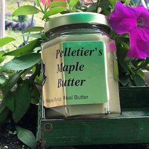 Könnte beinhalten: Ein Glasgefäß mit Pelletier's Maple Butter, mit einem grünen Deckel und einem goldenen Etikett. Das Etikett trägt die Aufschrift "Pelletier's Maple Butter" und "Real Butter". Das Gefäß steht auf einem grünen Spielzeug-LKW.