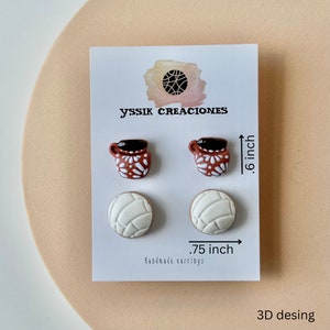 May include: A pair of earrings featuring two sets of designs: small brown mugs with white floral patterns and white concha bread shapes. The earrings are .6 inches and .75 inches in size. The card reads "yssik creaciones" and "Handmade earrings."