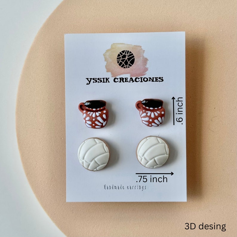 May include: A pair of earrings featuring two sets of designs: small brown mugs with white floral patterns and white concha bread shapes. The earrings are .6 inches and .75 inches in size. The card reads "yssik creaciones" and "Handmade earrings."