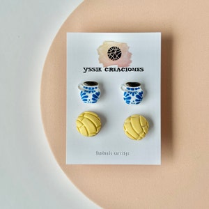 May include: A pair of handmade earrings on a white card. The earrings feature two pairs of miniature designs: blue and white coffee mugs and yellow concha bread. The card has the text "yssik creaciones" and "handmade earrings".