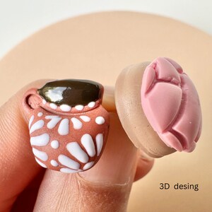 May include: A miniature terracotta-colored mug with white floral designs and a dark brown top. Next to it is a pink, heart-shaped object. The text "3D desing" is visible.