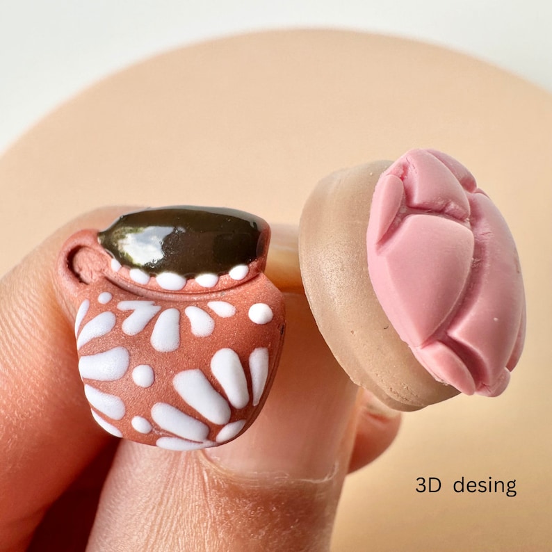 May include: A miniature terracotta-colored mug with white floral designs and a dark brown top. Next to it is a pink, heart-shaped object. The text "3D desing" is visible.