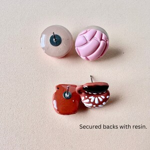 May include: Four stud earrings with resin-secured backs. Two are round, one pink and one nude. The other two are terracotta-colored, one shaped like a small pot and the other like a mug with white floral details.