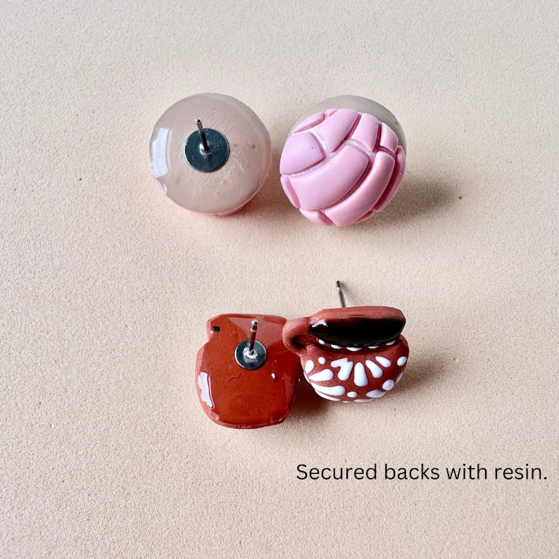 May include: Four stud earrings with resin-secured backs. Two are round, one pink and one nude. The other two are terracotta-colored, one shaped like a small pot and the other like a mug with white floral details.
