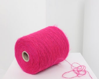 Pode incluir: Um rolo de fio rosa brilhante com uma textura felpuda. O fio está enrolado em torno de um tubo de cartão e um pedaço de fio está pendurado na ponta.