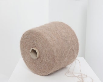 Pode incluir: Um rolo de fio de cor bege claro com um tubo de papelão no centro. O fio é macio e felpudo, perfeito para tricotar ou fazer crochê.