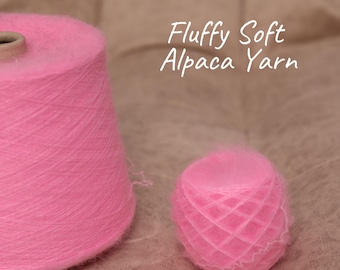 May include: Two pink alpaca yarn cones are shown. A large cone is on the left, and a smaller ball of yarn is on the right. The text "Fluffy Soft Alpaca Yarn" is in the upper right corner.