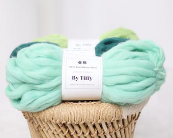 May include: Three skeins of 100% fine merino wool yarn in shades of green, teal, and mint. The yarn is arranged in a wicker basket. The label reads "100% Fine Merino Wool Handmade in Bulgaria By Tiffy www.thetiffymonroe.com"