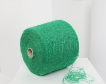 Pode incluir: Um rolo de fio verde brilhante com uma textura felpuda. O fio está enrolado em torno de um tubo de cartão e há uma ponta solta de fio pendurada no rolo.