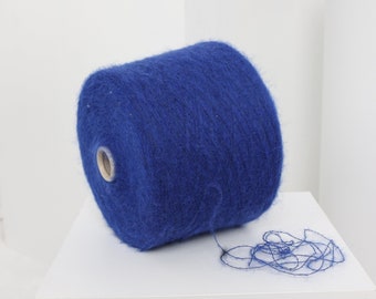 Pode incluir: Um novelo de lã azul com textura felpuda. A lã está enrolada em torno de um tubo de cartão e está pronta para ser usada para tricotar ou fazer crochê.