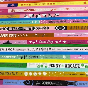 May include: A colorful, layered image featuring various horizontal bands with text and decorative elements. The bands display phrases like "eye candy," "Heirloom," and "Penny Arcade," along with designer names and dates. The overall design is vibrant and artistic.