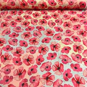 May include: Fabric with a repeating pattern of pink poppies with dark centers and white lace-like details. The background is a light blue and cream color with faint script writing. The fabric is rolled up.