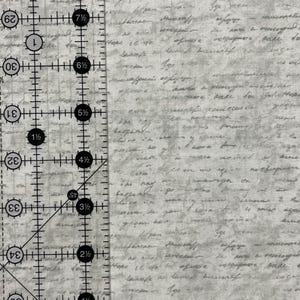 May include: A close-up of a white fabric with a gray and black printed pattern of handwritten text. A ruler with markings in inches is visible on the left side of the image.