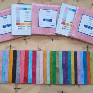May include: Fabric bundles in various colors, including pink, blue, and green, are displayed. The bundles are wrapped in clear plastic and have labels with the text "Fabrics" and "Thank You For Your Business." Below the bundles are fabric swatches in a variety of colors.